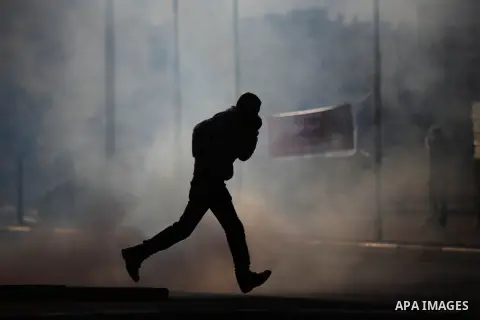 A Palestinian protester runs for cover from tear gas fired by Israeli security forces during clashes in Beit El on the outskirts of the West Bank city of Ramallah, Dec.12, 2015. Photo by Shadi Hatem