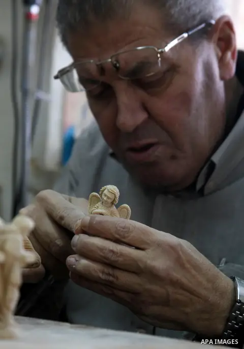 A Palestinian carpenter carves a wooden effigies of the the Holy Family at a workshop in the West Bank town of Bethlehem, on December 17, 2015. The traditional birthplace of Jesus Christ prepares to celebrate Christmas l...