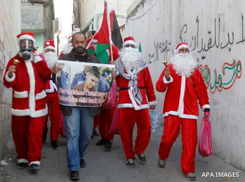 Palestinians dressed up as Santa Claus demonstrate in front of the Israeli controversial separation wall in the West Bank city of Bethlehem, on December 18, 2015. Photo by Wisam Hashlamoun