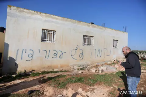 A Palestinian man stands next to a house sprayed with graffiti reading in Hebrew: "revenge" and "hello from the prisoners of Zion", in the village of Beitillu, near Ramallah in the Israeli occupied West Bank on December...