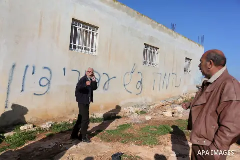 Palestinians gather next to a house sprayed with graffiti reading in Hebrew: "revenge" and "hello from the prisoners of Zion", in the village of Beitillu, near Ramallah in the Israeli occupied West Bank on December 22, 2...