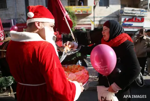 Palestinians dressed up as Santa Claus hand out gifts and sweets to the people at street to mark Christmas and Mawlid al-Nabi, the birthday of Prophet Mohammad in the West Bank city of Ramallah on Dec. 23, 2015. Photo by...
