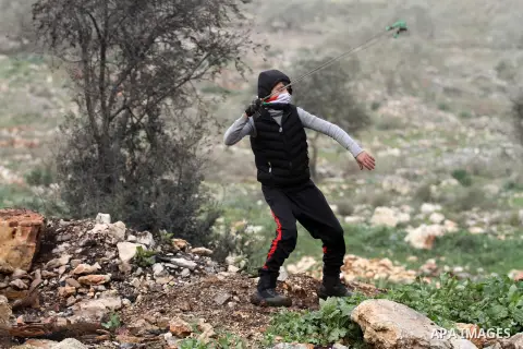 A Palestinian protester uses a slingshot to hurl stones toward Israeli security forces during clashes following a protest against the expropriation of Palestinian land by Israel in the West Bank village of Kafr Qaddum, n...