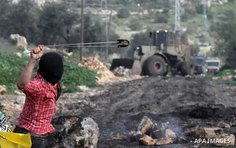 A Palestinian protester uses a slingshot to hurl stones toward Israeli security forces during clashes following a protest against the expropriation of Palestinian land by Israel in the West Bank village of Kafr Qaddum, n...