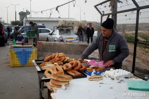 A Palestinian working in Israel buys food from a vendor as he waits to cross through the Israeli-controlled Mitar checkpoint south of the West Bank city of Hebron January 19, 2016. Photo by Wisam Hashlamoun