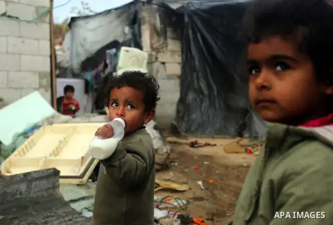 A Palestinian boy holds his milk bottle outside his family's dwelling on a rainy day, in Khan Younis in the southern Gaza Strip, January 24, 2016. Photo by Yasser Qudih