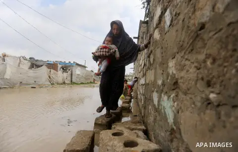 A Palestinian woman holds her son as she crosses a road flooded with rainwater following heavy rains, in Khan Younis in the southern Gaza Strip January 24, 2016. Photo by Yasser Qudih