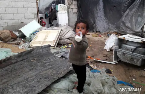 A Palestinian boy holds his milk bottle outside his family's dwelling on a rainy day, in Khan Younis in the southern Gaza Strip, January 24, 2016. Photo by Abed Rahim Khatib