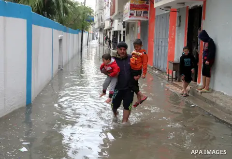 A Palestinian man holds his sons as he crosses a road flooded with rainwater following heavy rains, in Rafah in the southern Gaza Strip January 25, 2016. Photo by Abed Rahim Khatib