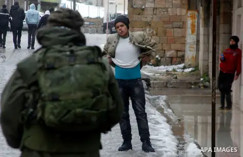 Israeli soldiers forces check Palestinians as they cross the street during a snowstorm in the West Bank city of Hebron, on January 26, 2016. Photo by Wisam Hashlamoun