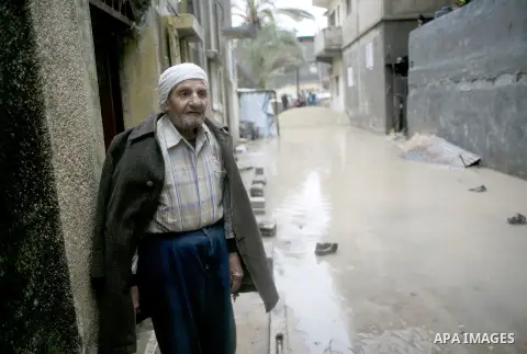 A Palestinian man stands on his doorstep looking at a flooded street following heavy rainfall in the southern Gaza Strip town of Rafah on January 26, 2016. Photo by Abed Rahim Khatib