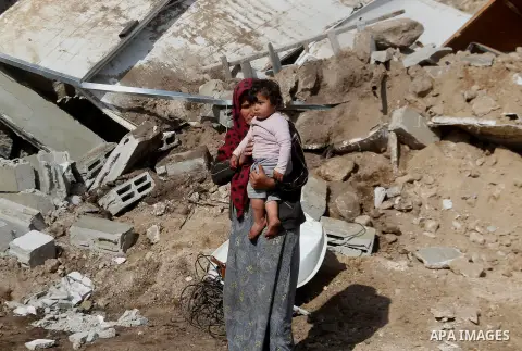 A Palestinian woman stands holding a child next to items salvaged from the remains of their home after it was demolished by Israeli bulldozers in a disputed military zone in the area of Musafir Jenbah, which includes sev...