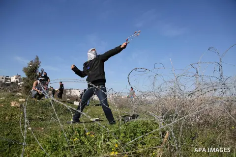 A Palestinian protester uses a slingshot to hurls stones toward israeli security forces during clashes following a demonstration in solidarity with Palestinian prisoners in Israeli jails, outside the compound of the Isra...