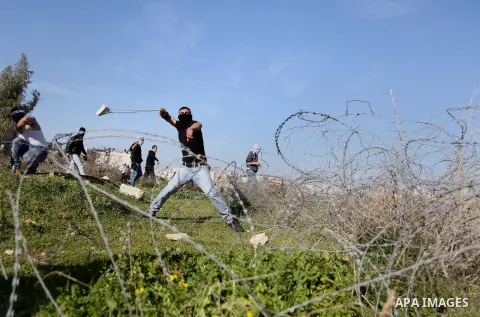 A Palestinian protester uses a slingshot to hurls stones toward israeli security forces during clashes following a demonstration in solidarity with Palestinian prisoners in Israeli jails, outside the compound of the Isra...