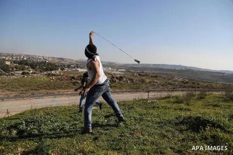 A Palestinian protester uses a slingshot to hurls stones toward israeli security forces during clashes following a demonstration in solidarity with Palestinian prisoners in Israeli jails, outside the compound of the Isra...