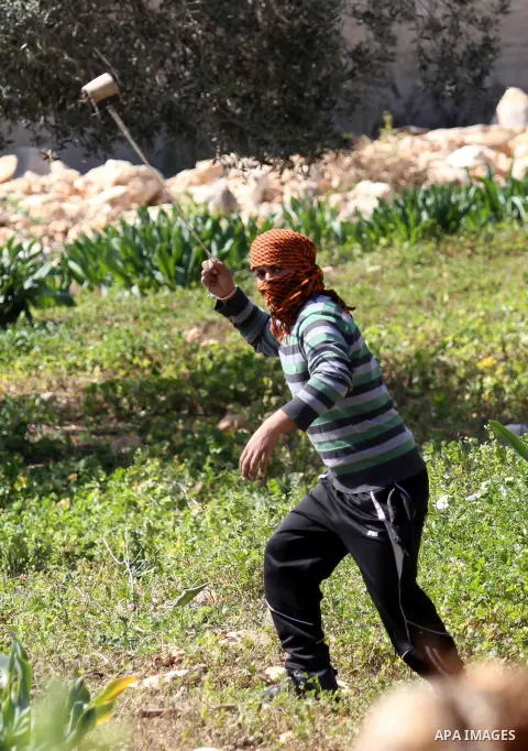 A Palestinian protester uses a slingshot to hurl stones towards Israeli security forces during clashes following a demonstration against the expropriation of Palestinian land by Israel on February 19, 2016 in the village...