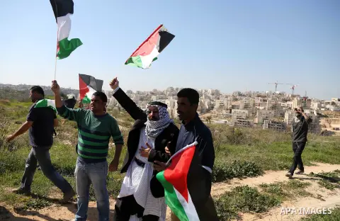 Palestinians hold national flags during clashes with Israeli security forces following a march on February 19, 2016 in the West Bank village of Bilin, near Ramallah, to mark the 11th anniversary of their uprising against...