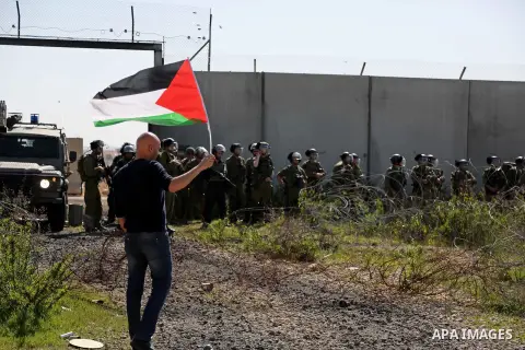 A Palestinian man holds national flags during clashes with Israeli security forces following a march on February 19, 2016 in the West Bank village of Bilin, near Ramallah, to mark the 11th anniversary of their uprising a...