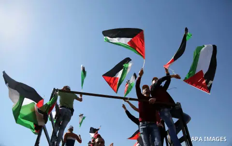 Palestinians hold national flags during clashes with Israeli security forces following a march on February 19, 2016 in the West Bank village of Bilin, near Ramallah, to mark the 11th anniversary of their uprising against...
