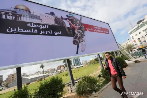 Palestinians walk past a placard depicting a member of the Ezzedine al-Qassam Brigades, the armed wing of the Hamas movement in Gaza city on March 20, 2016. Photo by Mohammed Asad