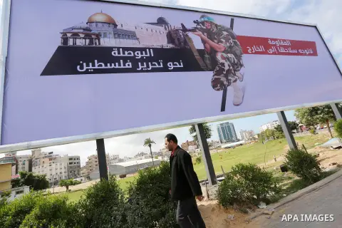 Palestinians walk past a placard depicting a member of the Ezzedine al-Qassam Brigades, the armed wing of the Hamas movement in Gaza city on March 20, 2016. Photo by Mohammed Asad