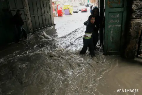 Palestinians walk in a street flooded by rain water in the West Bank city of Hebron, on March 28, 2016. Photo by Wisam Hashlamoun