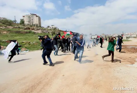 Palestinian journalists run for cover from tear gas fired by Israeli security forces during a demonstration to mark Land Day outside the compound of the Israeli-run Ofer prison near Betunia in the Israeli occupied West B...