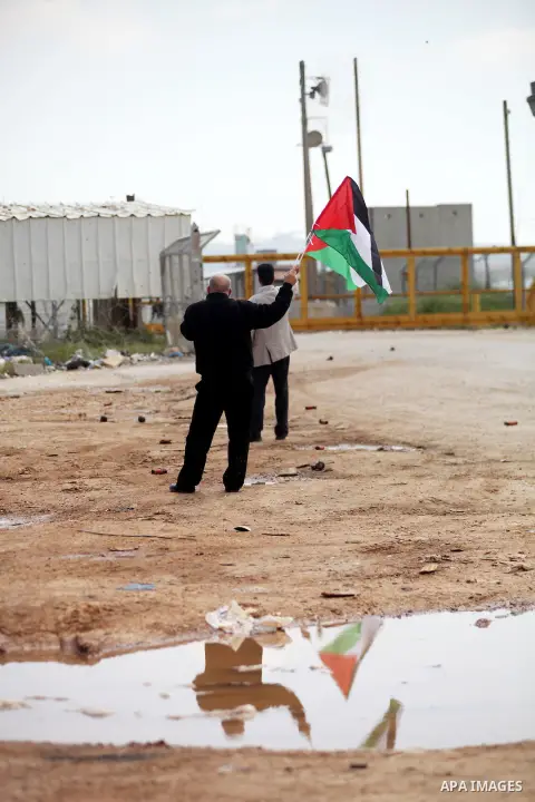 Palestinian protesters wave their national flag in front of Israeli security forces as they mark Land Day outside the compound of the Israeli-run Ofer prison near Betunia in the Israeli occupied West Bank on March 30, 20...