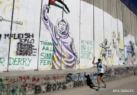 A participant runs past the controversial Israeli barrier during the annual Right to Movement Palestine Marathon in the West Bank town of Bethlehem April 1, 2016. Photo by Wisam Hashlamoun
