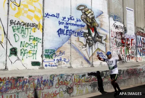 A participant runs past the controversial Israeli barrier during the annual Right to Movement Palestine Marathon in the West Bank town of Bethlehem April 1, 2016. Photo by Wisam Hashlamoun