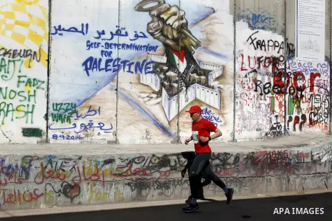 A participant runs past the controversial Israeli barrier during the annual Right to Movement Palestine Marathon in the West Bank town of Bethlehem April 1, 2016. Photo by Wisam Hashlamoun