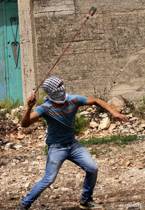 A Palestinian protester uses a slingshot to hurl stones towards Israeli security forces during clashes following a weekly demonstration against the expropriation of Palestinian land by Israel in the village of Kfar Qaddu...