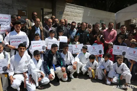 Palestinians hold banners during a protest in solidarity with the karate trainer, Hassan El-Raey against his arrest by the Israeli army, in front of Red cross office in Gaza city on April 13, 2016. Photo by Mohammed Asad