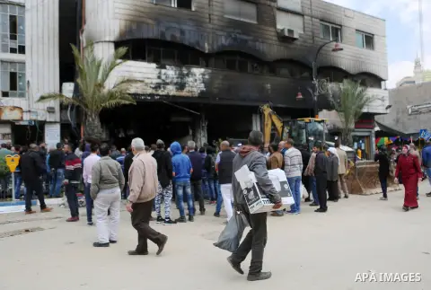 Palestinians gather around a money changer in the Palestinian political capital Ramallah after it was raided by Israeli forces, blowing up a safe and sparking a fire, on April 14, 2016. An Israeli army spokeswoman said t...