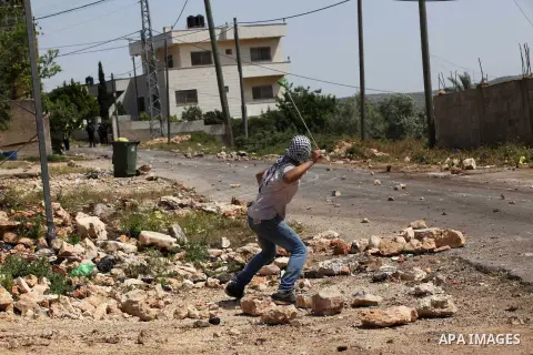 A Palestinian protester uses a slingshot to hurl stones towards Israeli security forces during clashes following a weekly demonstration against the expropriation of Palestinian land by Israel in the village of Kfar Qaddu...