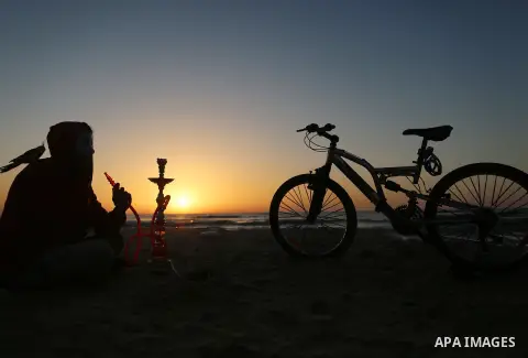 A Palestinian youth smokes flavoured tobacco water pipes or 'shisha' during sunset at the beach of the Mediterranean sea on the coast of Gaza city on April 17, 2016. Photo by Yasser Qudih
