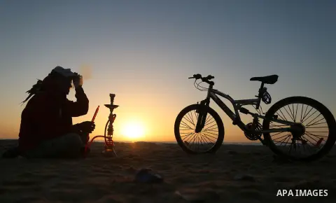 A Palestinian youth smokes flavoured tobacco water pipes or 'shisha' during sunset at the beach of the Mediterranean sea on the coast of Gaza city on April 17, 2016. Photo by Yasser Qudih