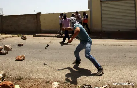 A Palestinian protester uses a slingshot to hurl stones towards Israeli security forces during clashes following a weekly demonstration against the expropriation of Palestinian land by Israel in the village of Kfar Qaddu...