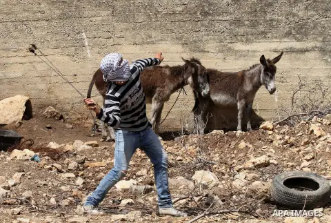 A Palestinian protester uses a slingshot to hurl stones towards Israeli security forces during clashes following a weekly demonstration against the expropriation of Palestinian land by Israel in the village of Kfar Qaddu...