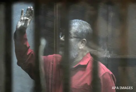 Egypt's ousted Islamist president Mohamed Morsi, wearing a red uniform, gestures from behind the bars during his trial at the police academy in Cairo on April 23, 2016. An Egyptian court postponed its verdict and sentenc...