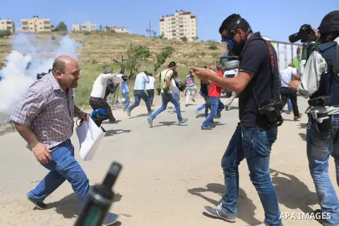 Palestinian journalists run for cover from a tear gas canister fired by Israeli troops during a protest calling for the release of Palestinian journalist Omar Nazal, who is held by Israel, near Israel's Ofer Prison near...