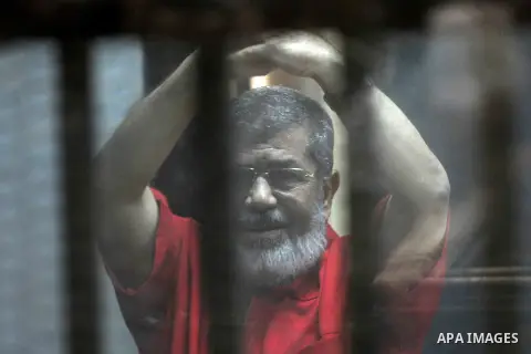 Egypt's ousted Islamist president Mohamed Morsi, wearing a red uniform, gestures from behind the defendant's bars during his trial at the police academy in Cairo on May 7, 2016. An Egyptian court recommended death senten...