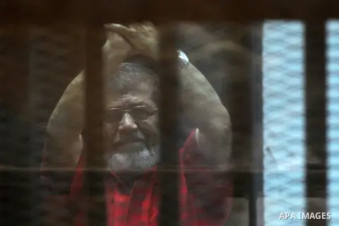 Egypt's ousted Islamist president Mohamed Morsi, wearing a red uniform, gestures from behind the defendant's bars during his trial at the police academy in Cairo on May 7, 2016. An Egyptian court recommended death senten...