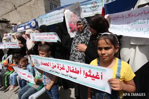 Palestinian children hold placards during a protest against the killing of three boys from the al-Hindi family, who died in a fire caused by a candle at the family home in Gaza city on May 9, 2016. Photo by Ashraf Amra