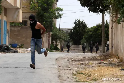 A masked Palestinian protester runs for cover during clashes with Israeli security forces following a demonstration against the expropriation of Palestinian land by Israel, on May 13, 2016 in the village of Kfar Qaddum,...