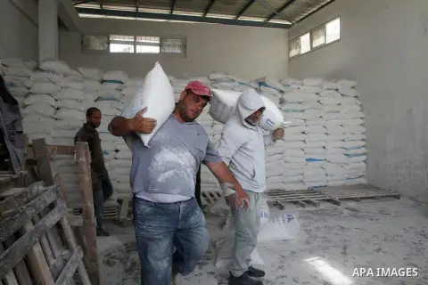 Palestinian workers carry bags of flour to distribute to families, at an aid distribution centre of the United Nations Relief and Works Agency (UNRWA) in the southern Gaza Strip town of Khan Younis on May 15, 2016, on th...
