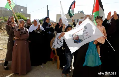 Palestinians wave national flags on May 19, 2016 in the southern West Bank village of Dura, as they wait for the arrival of Palestinian imprisoned journalist, Mohammed al-Qiq, after he was released from the Israeli Nafha...