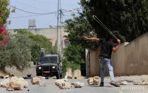 A Palestinian protester uses a slingshot to throw stones towards Israeli security forces during clashes following a demonstration against the expropriation of Palestinian land by Israel, on May 20, 2016 in the village of...