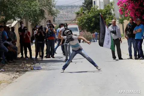 A Palestinian protester uses a slingshot to throw stones towards Israeli security forces during clashes following a demonstration against the expropriation of Palestinian land by Israel, on May 20, 2016 in the village of...