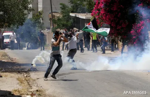 Palestinian protesters take cover from tear gas fired by Israeli security forces during clashes following a demonstration against the expropriation of Palestinian land by Israel, on May 20, 2016 in the village of Kfar Qa...